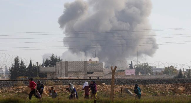 Syrians run for cover as smoke rises over the Syrian town of Ras al-Ain after an air strike, as seen from the Turkish border town of Ceylanpinar