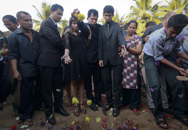 Jacintha Saldanha's widower Barboza and her children Lisha and Junal throw flowers on her grave during her funeral at a cemetery in Shirva