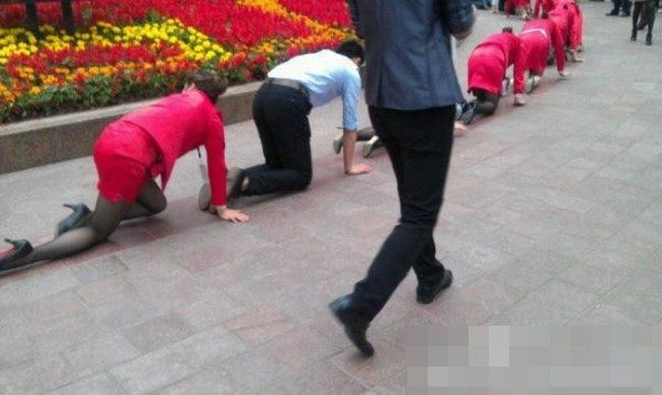 Chongqing bölgesindeki Yuzhong şehrinde bir grup üniformalı çalışan dizleri üzerinde yürüyüş yaparken görülüyor.
