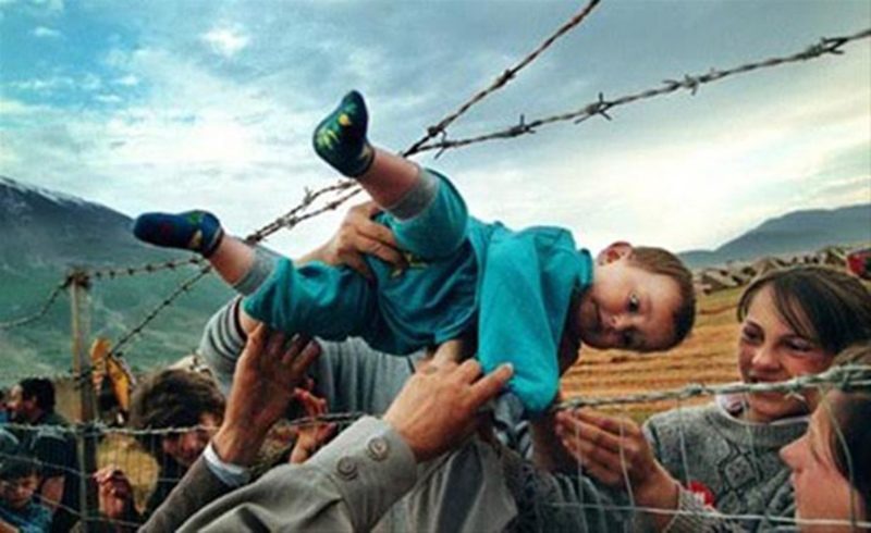 Arnavut mülteci kampında ailesi ile birlikte tutulan iki yaşındaki Kosovalı mülteci çocuğun çitler arasından ailesine uzatıldığı fotoğraf zamanın simge olmuş görüntülerinden biri.