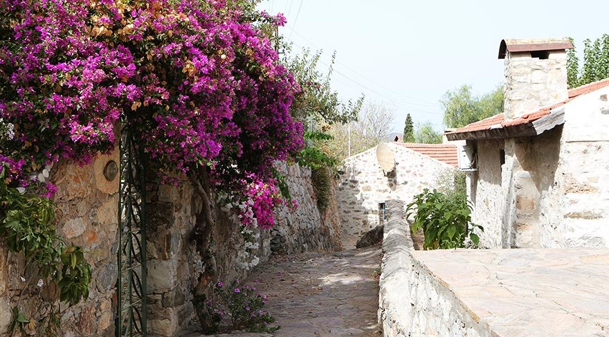 Taş döşeli dar sokakları, duvarları süsleyen mor, pembe, beyaz ve fuşya begomvilleri ve rengarenk bahçe çiçekleriyle gidenleri adeta içine çekiyor.